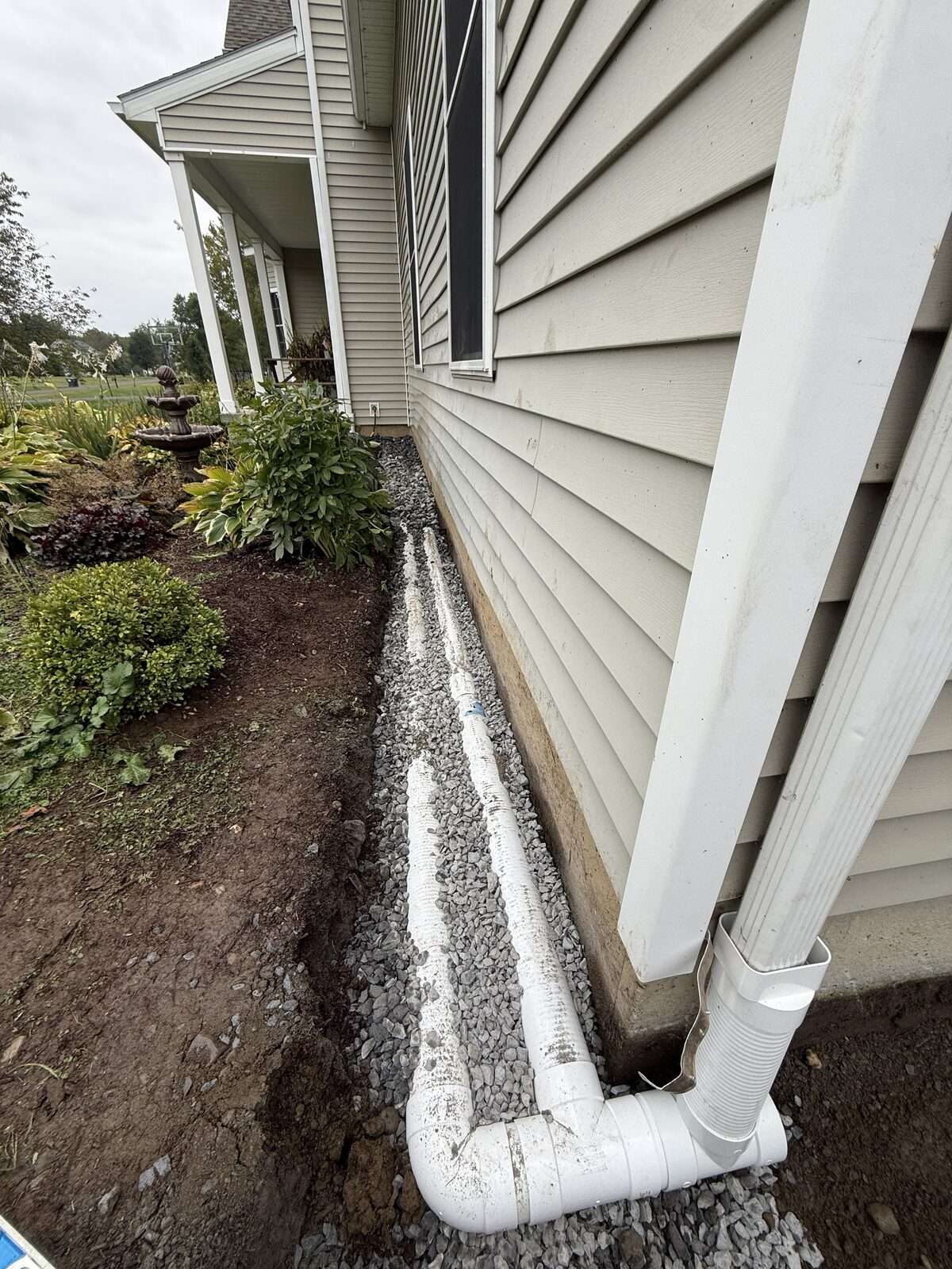Perforated french drain pipe and a separate solid downspout line bedded in stone along a house foundation in Valatie NY